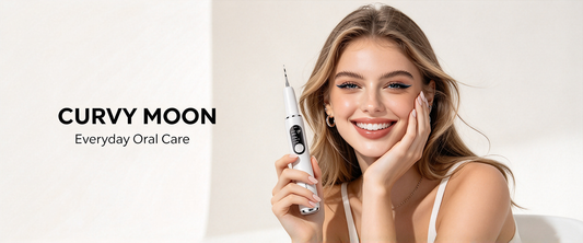 Smiling woman with long wavy hair resting her cheek on one hand and holding a white Curvy Moon handheld dental cleaner beside her face.